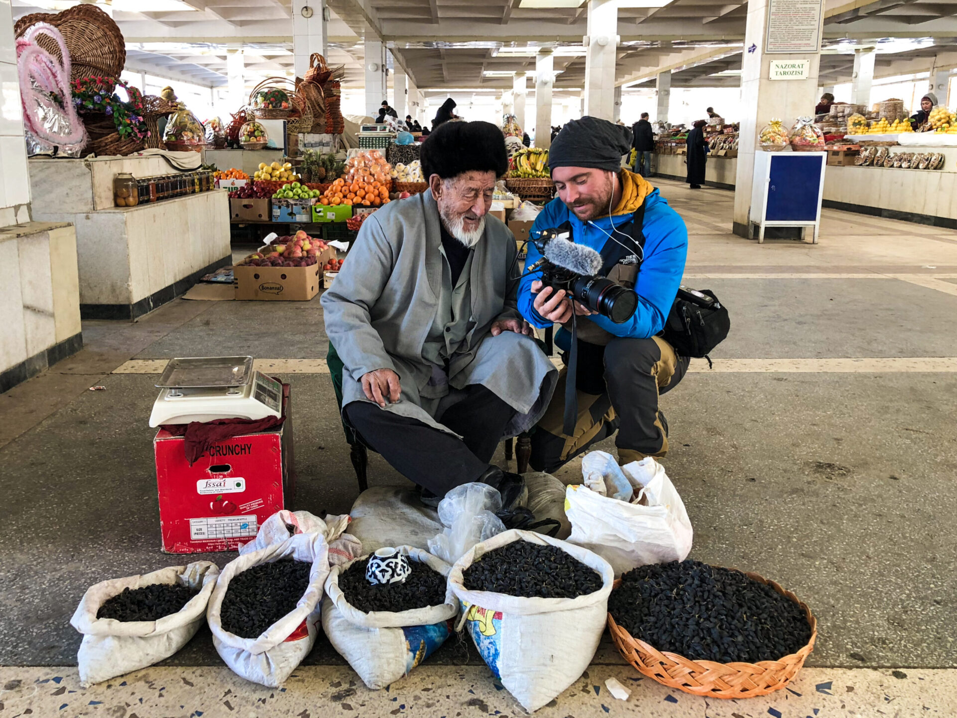 Brent Gundesen on shoot showing the footage to an elderly man in a market